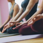 Exercise and mental health - Women practicing yoga together and sitting in the lotus pose: mindfulness meditation, spirituality and healthy lifestyle concept