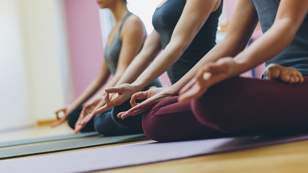 Exercise and mental health - Women practicing yoga together and sitting in the lotus pose: mindfulness meditation, spirituality and healthy lifestyle concept
