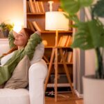 Woman relaxing on a white couch at home, eyes closed and hands behind her head, enjoying a peaceful moment of rest.