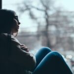 Silhouette of sad teenage girl looking out the window