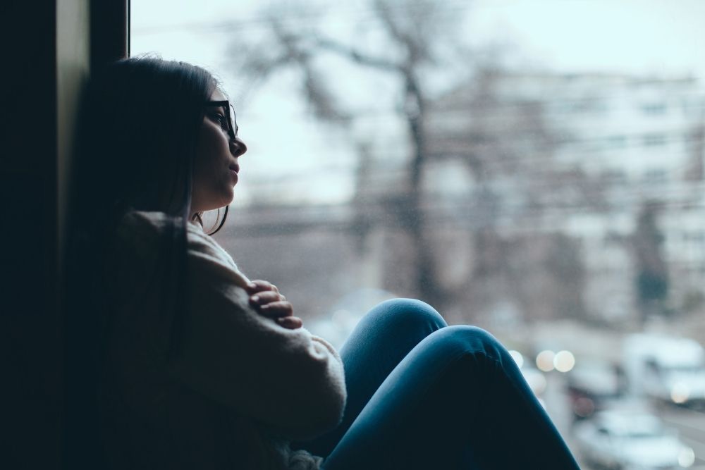 Silhouette of sad teenage girl looking out the window