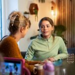Teen girl talking with an adult at a table in a cozy home setting, appearing engaged in a serious conversation