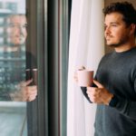 man drinking coffee and looking out his window