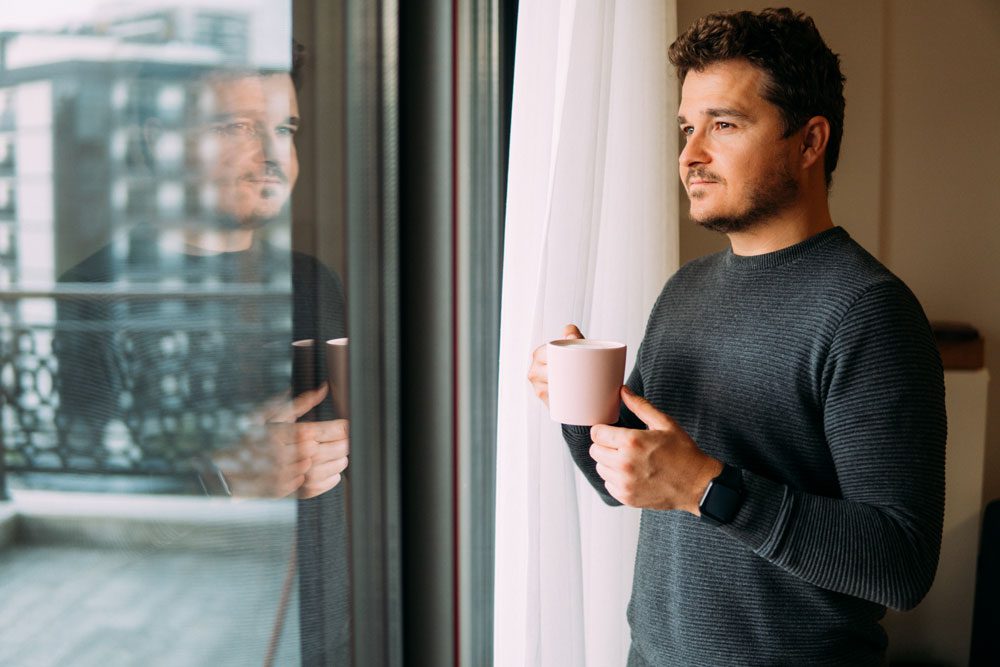 man drinking coffee and looking out his window