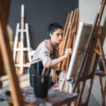 Person painting on an easel in an art studio - recognizing the benefits of creative expression on their mental health.